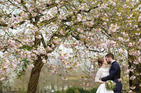 Bride wearing lace wedding dress with peter pan collar at East Riddleden Hall kissing under blossoms