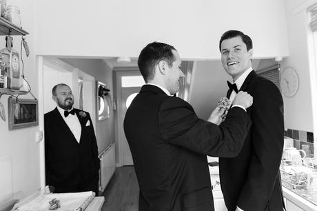 Groom wearing a tuxedo with best man putting on a buttonhole