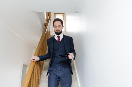 Groom with beard walking down stairs wearing blue suit red tie