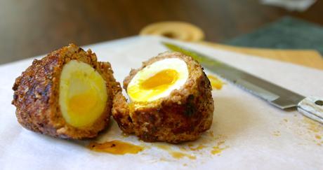 a scotch egg cut in half on a plate with a knife in the background