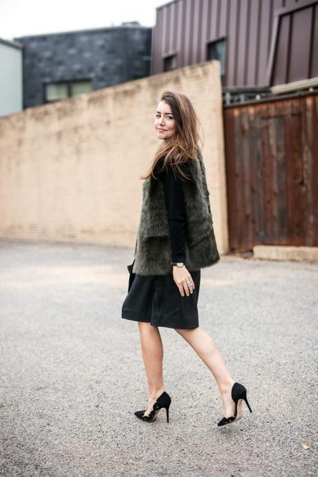 Amy havins wears a leather skirt with a green fur vest and black heels.