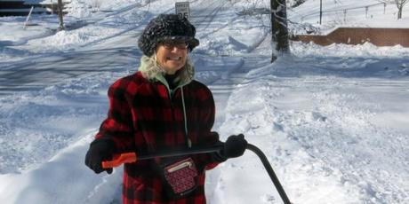 Woman holding shovel smiling while shoveling snow