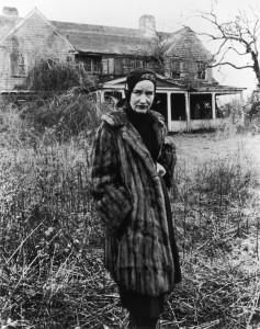 Little Edie shown in a typical Edie juxtaposition; posing ironically in a fur coat in front of the decrepit shambles the Grey Gardens property was in.