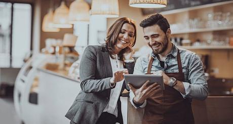 Shot of a smiling cafe owner  and employee barista standing inside a coffee shop looking at new menu on a digital tablet