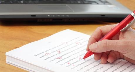 Close-up of a hand proofreading a manuscript with a red pen