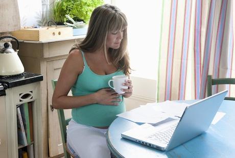pregnant woman drinking coffee in front of laptop
