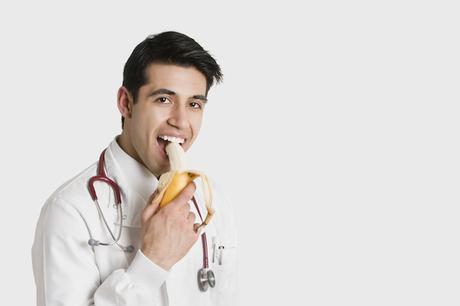 Indian male doctor eating banana over white background