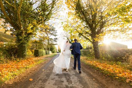 Bride and groom walking up the street in the autumn at The Normans