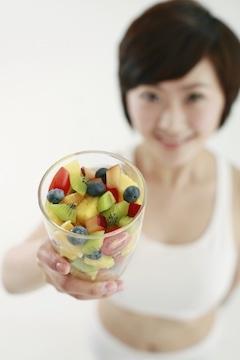 Woman holding a glass of mixed fruits high in polyphenols, focus on foreground