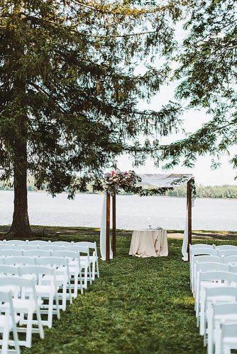wedding ceremony decorations on the bank of the river with white chairs and a beautiful arch decorated with flowers of roses and greens air cloth pat furey photography