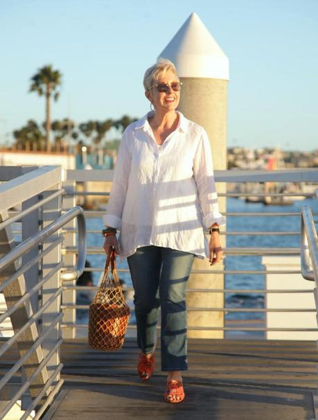 style blogger Susan B wears an easy white shirt with jeans, a Staud bucket bag and orange sandals. Details at une femme d'un certain age.