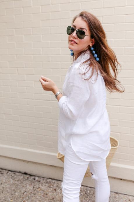 Amy Havins wears white jeans and a white blouse with statement earrings.