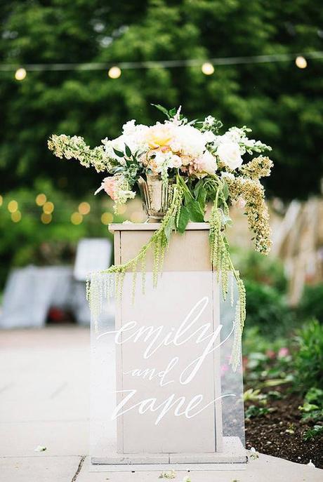 acrylic sign leaning against wedding alter with floral arrangement