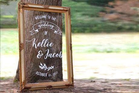 acrylic wedding sign framed in a gold gilded frame leaning against a tree