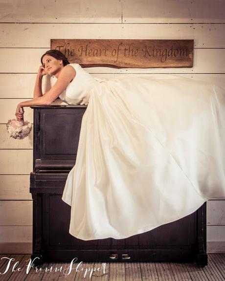 Bride casually laying on a piano at Bashall Hall in her big wedding dress holding a unicorn inspired Bouquet