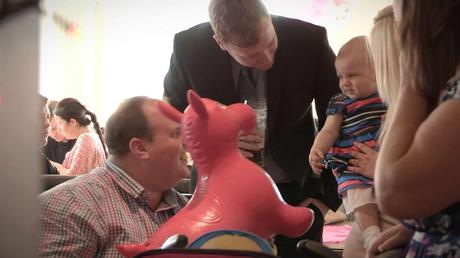 parents trying to make a baby girl laugh with an inflatable horse at a christening in rhyl