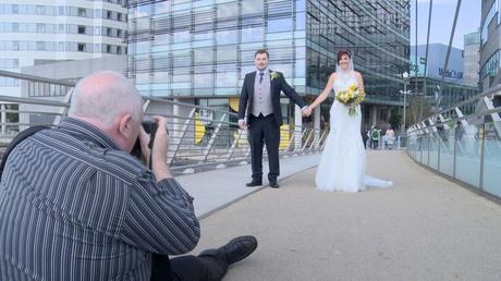Mick Cookson sits on the floor of lowry bridge to take a fun photo of the bride and groom