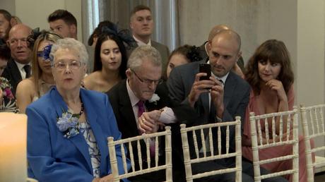 wedding guests check their watches and take photos on their phones as they wait for the Bride to arrive for a wedding inside the members club On The 7th