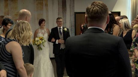 Our short haired bride walks down the aisle with her dad holding a sunflower and white rose bouquet 