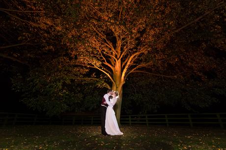 Bride and groom kiss under tree lit by