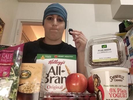 The author surrounded by salad, oatmeal, all-bran cereal, apples, raspberries, yogurt, and flax seeds, and additionally holding a prune.