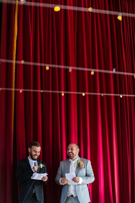 Grooms giving speeches in front of red curtain
