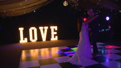 a bride and groom do their first dance for the wedding video on a black and white dance floor with illuminated LOVE letters behind them