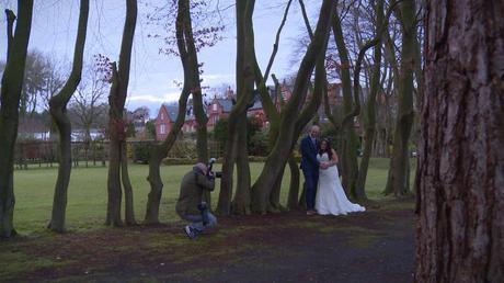 a wedding photographer crouches down to take a photo of the bride and groom posing outside Nunsmere Hall on a chilly December day