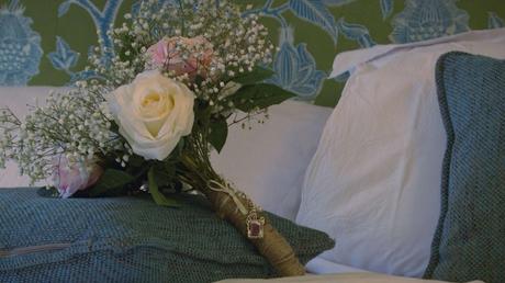 A silk flower bouquet of pinks and creams with gypsy grass lays on the green pillow. It's hand tied with brown string and has a pendant of the brides dad to remember him on her wedding day