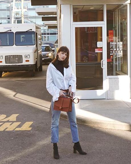 White button down shirt styled with blue jeans and black boots, tan handbag. Courtesy Saskaludilo