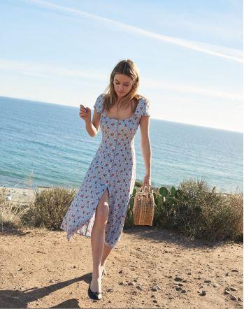 Printed blue summer dress with a slit in front styled with tan straw bag near sea that makes it perfect pic. Courtesy Reformation