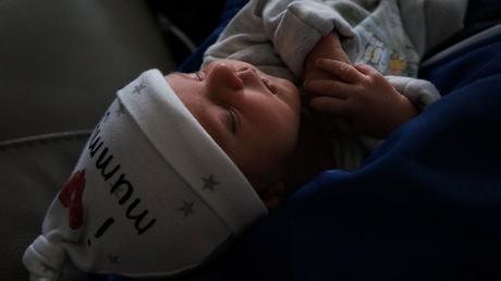 newborn baby girl being held in a mans arms wearing a cute I love Mummy hat and sleeping in a house in Newark