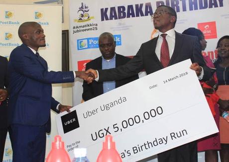 Aaron Tindie, country manager for Uber Uganda, hands a check to the Katikkiro of Buganda, Peter Mayiga