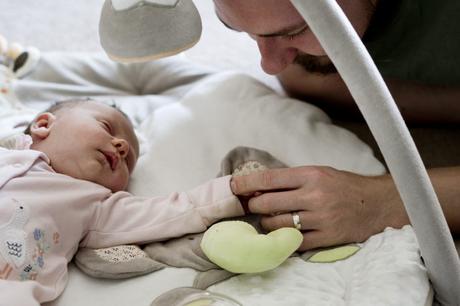 daddy and newborn daughter hold hands as she lays on her neutral coloured play mat in their living room in Lancashire for their family photographer