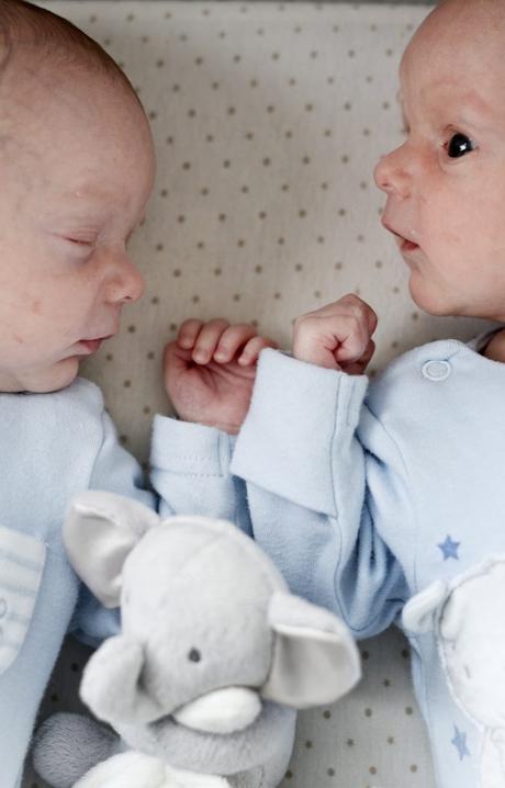 a gorgeous close up image of twin boys born premature in their cot. one is sleeping and the other alert as they touch hands
