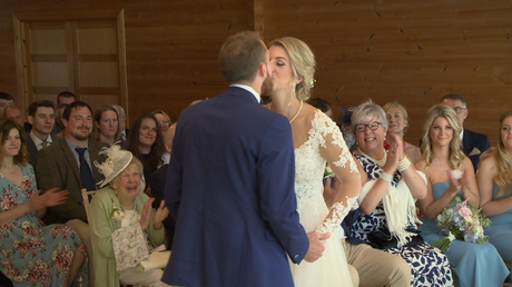 the moment when they say you may kiss the bride and the guests are smiling and clapping behind them at Styal Lodge in Cheshire