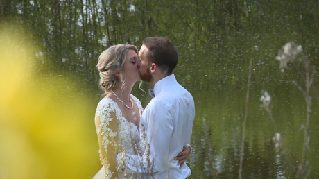 a bride and groom have a kiss on the jetty in front of the lake at Styal Lodge in Cheshire