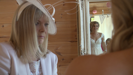 mother of the bride checks the final fitting of her daughter in her wedding dress as she smiles at herself in the floor length silver mirror in styal lodges bridal room