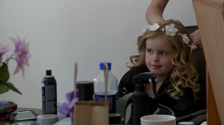 a young flower girl has a white flower crown added to her curled hair by the hair dresser for her Mum's wedding in Burscough