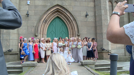 laura wade the wedding photographer ducks down to get a large group shot outside st johns churchs green doors