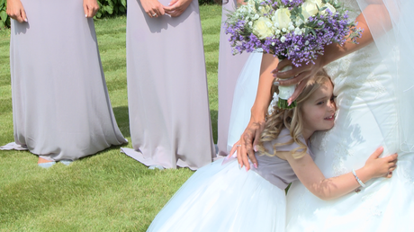 a flower girl gives her Mum in her wedding dress a big cuddle as the bridesmaids smile standing in her parents garden in Holmeswood