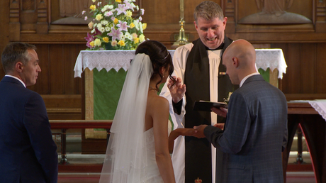 the priest at St Johns church makes a ting sign with his fingers to show the groom how to push the wedding ring on