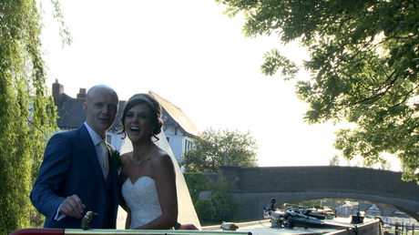 the bride laughs at the wedding videographer as they finish posing on the canal boat by burscough wharf