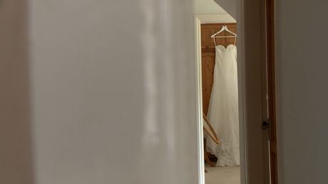 a lace wedding dress hangs on a wardrobe in a far room