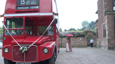 two bridesmaids hide under a red umbrella as they try to walk from the vintage london bus to the front door at Inglewood manor