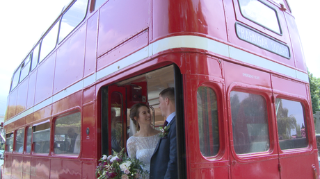 a bride and groom laugh with the photographer and videographer stood on the back of their vintage red london bus for photos in liverpool