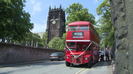 a vintage red double decker london bus with white wedding ribbon on is parked outside St Peters church in woolton on a summers day