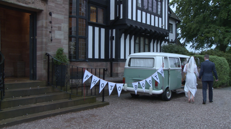 dusty the campervan photbooth is parked up as the bride and groom walk over outside inglewood manor