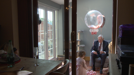 a grandad plays with balloons for a little flower girl dressed in pink