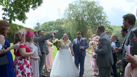 the bride laughs as she's showered in confetti holding her grooms hand alongside the lake at thornton manor